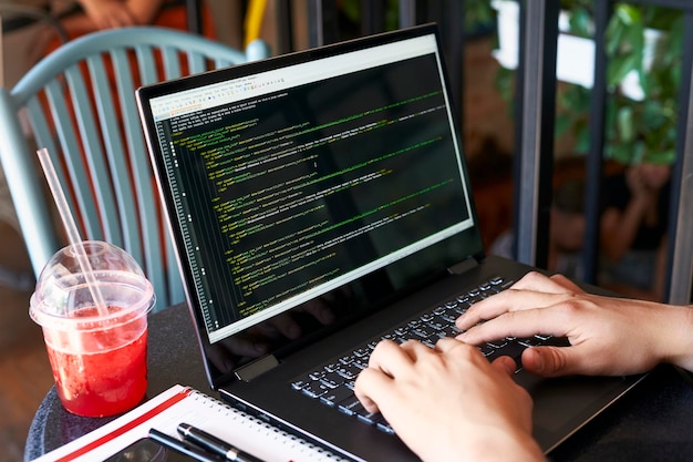 Developer programmer with laptop program code and script data\
on screen young freelancer in glasses working on project in cafe\
back view over the shoulder shot