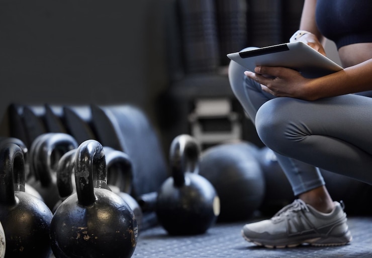 Photo developing a new circuit for her clients closeup shot of an unrecognisable woman using a digital tablet alongside kettlebells in a gym