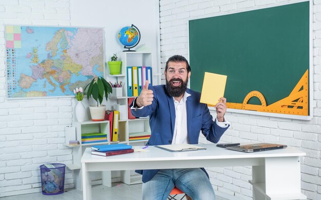 ひげを生やした主題の幸せな男を学ぶ開発は、レッスンが試験に合格する間、学校の教室に座っている非公式の教育を勉強する際のノートブックの進歩を見る