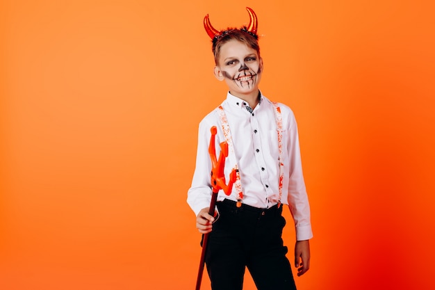 Devil boy standing halfturn against an orange  in masquerade makeup. Halloween 