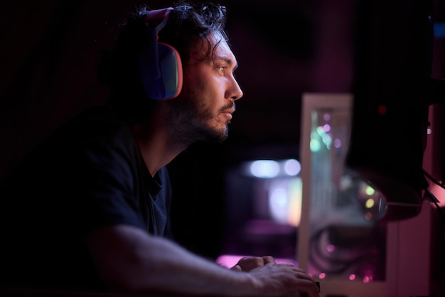 献身的なゲーマーが激しいゲームプレイに完全に没頭して活発なネオン照明の部屋に座っています