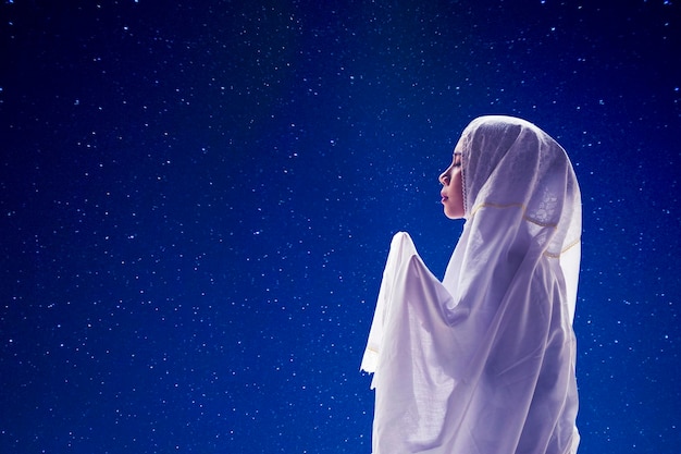 Devout woman praying to the Allah with stars in sky