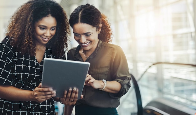 Deze app werkt perfect voor ons Bijgesneden opname van twee aantrekkelijke zakenvrouwen die samen een digitale tablet gebruiken terwijl ze op een moderne werkplek staan