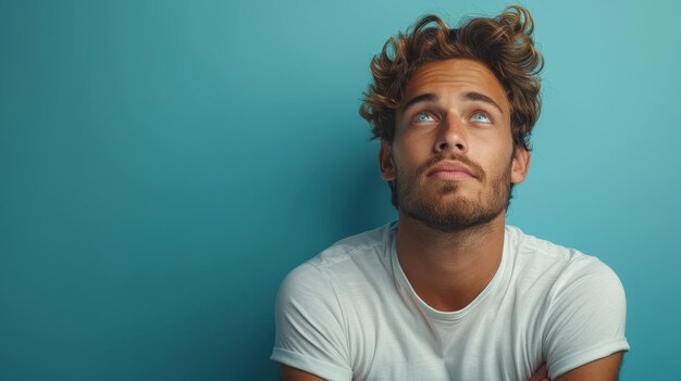 Foto deze gelukkige man bidt met gekruiste vingers naar de hemel kijkend met een smeekend gezicht tegen een blauwe achtergrond en maakt een wens