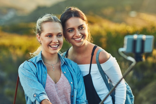 Deze selfie met een prachtig landschap wordt gedeeld Bijgesneden opname van twee mooie vriendinnen die een selfie maken met een selfiestick in de natuur