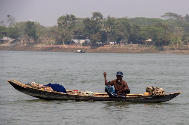 Dhaka Bangladesh march122023 Rural fisherman with a small wooden boat fishing on the river Scenic rural life closeup with an old fisherman and village background Beautiful southeast