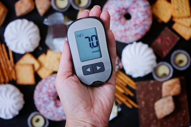 Foto concetto di diabete: dolci e cibo malsano con glucometro in mano. la nutrizione causa la malattia diabetica