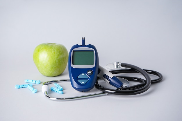 Diabetes concept with digital glucometer, lancet pen, stethoscope and apple