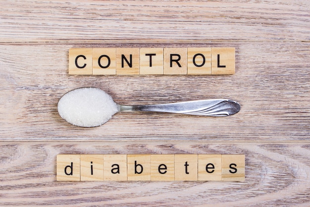 Le lettere di legno del blocco di controllo del diabete e lo zucchero ammucchiano su un cucchiaio