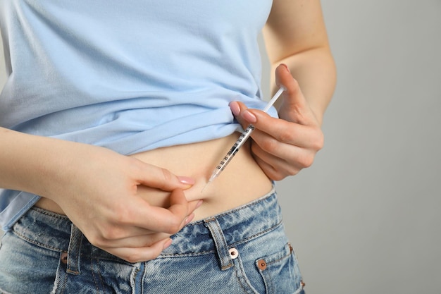 Diabetes Woman making insulin injection into her belly on grey background closeup