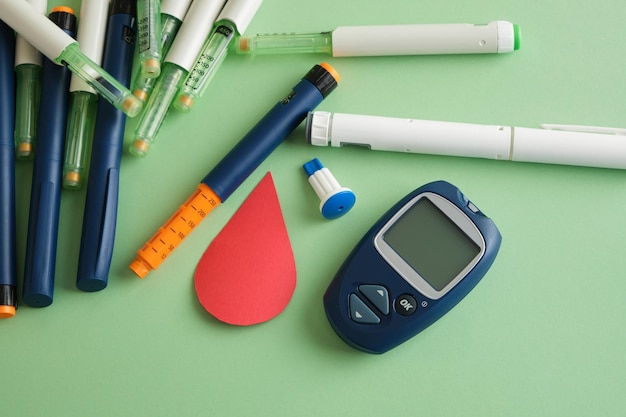 Diabetesconcept een apparaat om bloedsuiker te meten een papieren bloeddruppel en veel spuitpennen met insuline