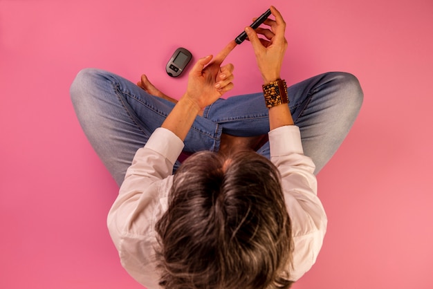 Diabetic woman sitting on the floor using devices to measure blood glucose.