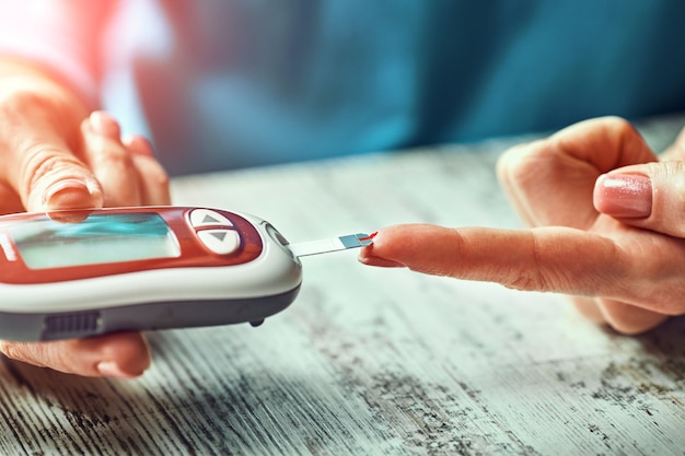 Diabetic woman using blood glucose meter, female hands hold lancet pen glucometer on finger measure sugar check insulin