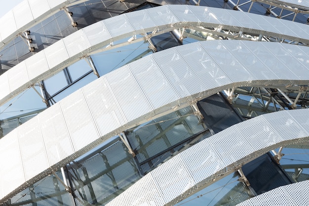 Diagonaal aanzicht van hoge moderne bouwconstructie met metalen geperforeerd paneel met ronde gaten en ramen. Hoek van modern gebouw