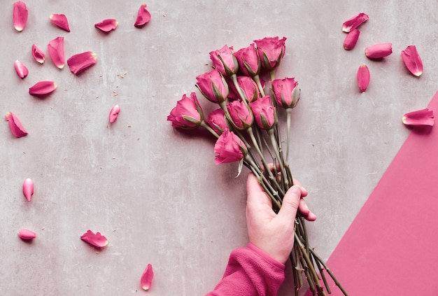 Diagonal geometric paper background on stone. Flat lay, female hands holding pink roses, scattered petals, Valentine day.