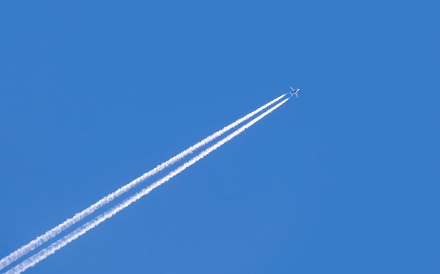 澄んだ青い空を飛んでいる飛行機の斜めの痕跡