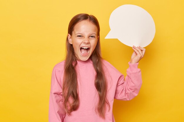 Dialog in an empty speech bubble creative idea on a blank card excited amazed little girl with long hair holding empty speech bubble wearing pink sweatshirt isolated over yellow background