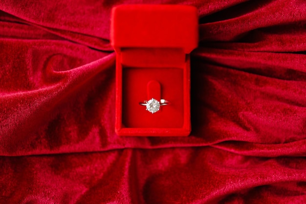 Diamond ring in jewelry gift box on red fabric background