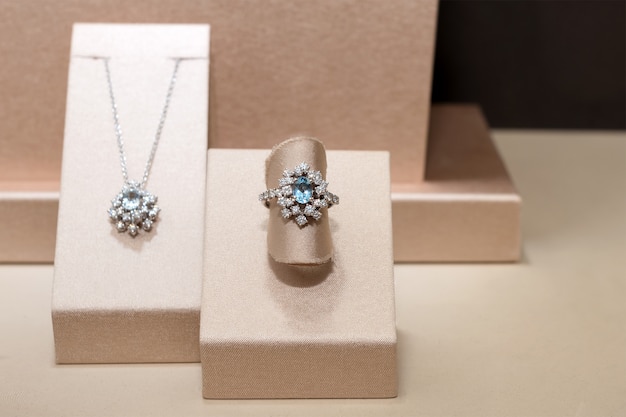Diamond ring and necklace with blue precious gems. White golden ring on stand. Fashion luxury accessories