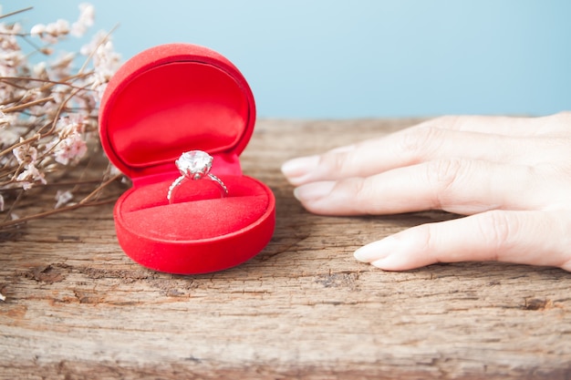 Foto anello di diamanti in scatola rossa con la mano della donna sul tavolo in legno, anello di fidanzamento, san valentino