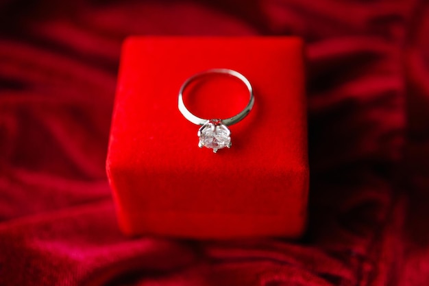Diamond ring with jewelry gift box on red fabric background