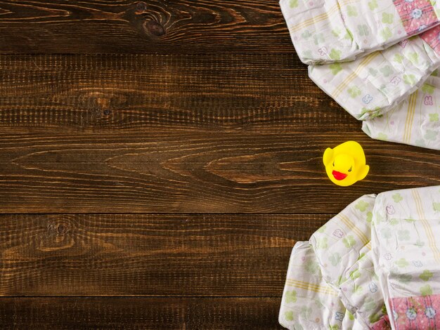 Diapers and rubber duckling on wooden background