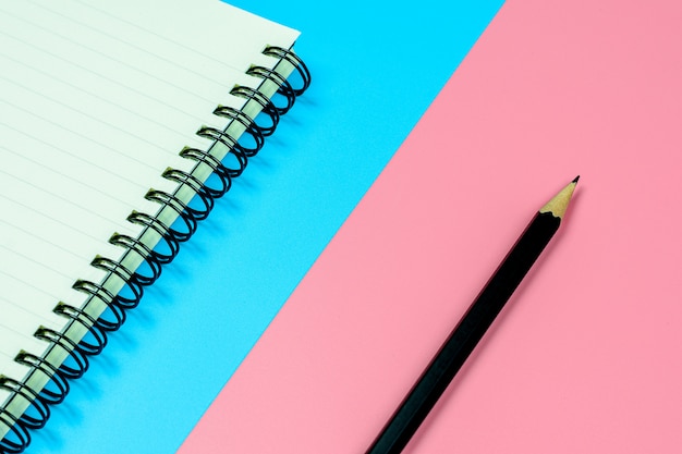 Diary book and a pencil on blue and pink background with copy space.