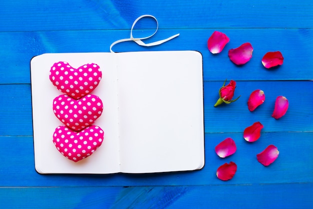 Diary notebook with rose and valentine's hearts on blue wooden background. 