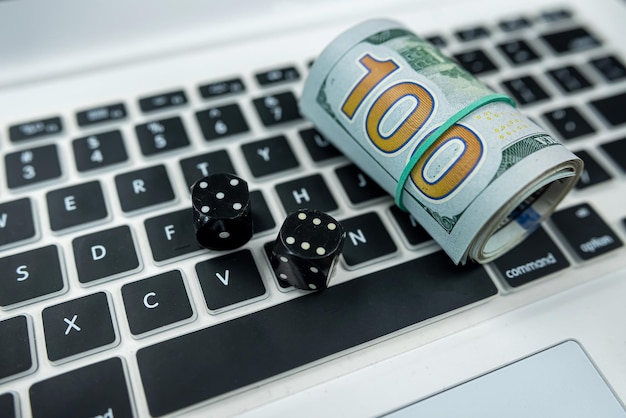 Dice and dollar bills on a new laptop keyboard isolated on a black table