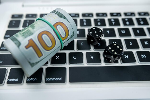 Dice and dollar bills on a new laptop keyboard isolated on a black table