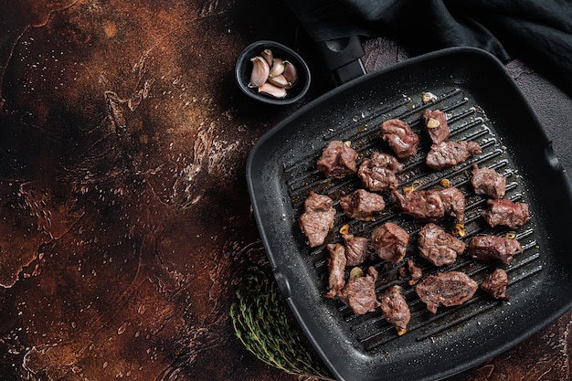 Diced beef cubes roasting in a grill pan for stew or goulash. Dark background. Top view. Copy space.