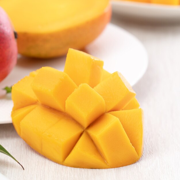 Foto frutto di mango fresco a dadini su un piatto bianco con foglie su sfondo di tavolo in legno