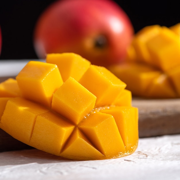 Diced fresh mango fruit on wooden cutting board with sunlight and leaf shadow at home kitchen in the afternoon