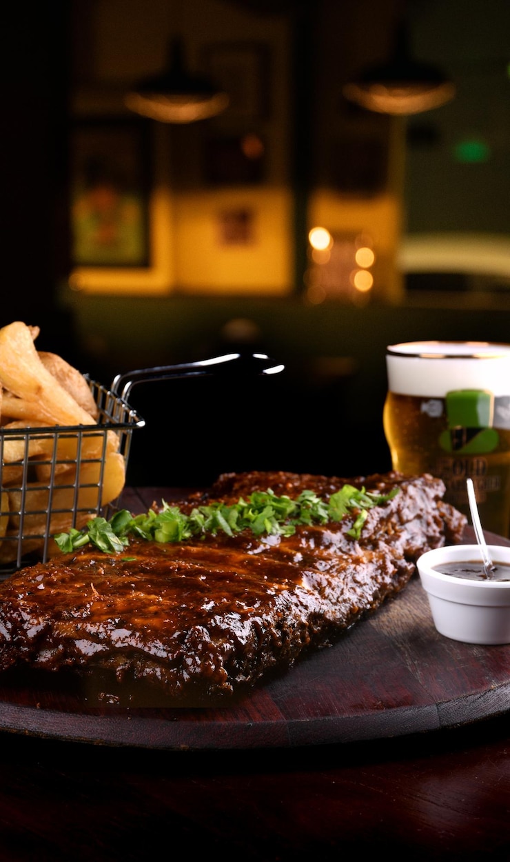 Foto dicht van varkensribbetjes in barbecue saus met peterselie met een mandje rustieke aardappelen en bbq saus met bier