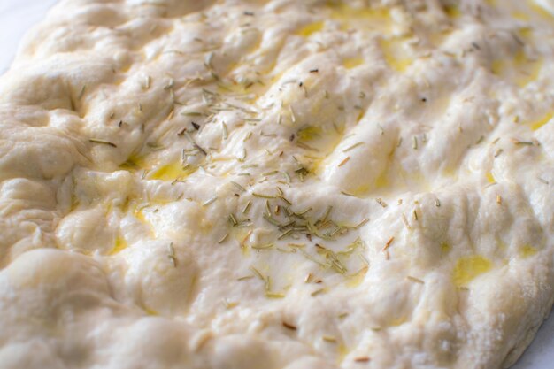 Dichtbijbeeld van typisch Italiaans Focaccia Brooddeeg met olie en rozemarijn zonder bakken