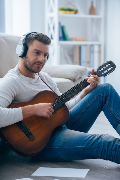 Die melodie spelen. Knappe jonge man in koptelefoon gitaarspelen