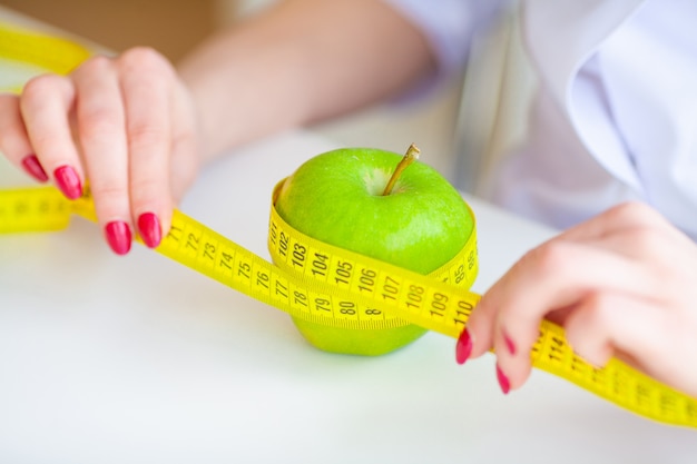 Dieet. fitness en gezond voedsel dieet concept. uitgebalanceerd dieet met groenten. portret van vrolijke artsenvoedingsdeskundige die groene appel in haar bureau meten. concept natuurlijk voedsel en gezonde levensstijl.