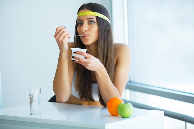 Dieet Gelukkige jonge vrouw die yoghurt eet in de keuken