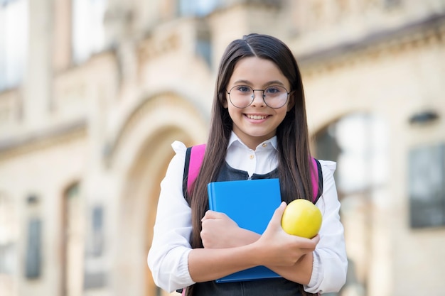 Dieet geneest meer dan dokters. Gelukkig schoolmeisje houdt appel en boek vast. Schoolpauze. Fruitsnack. Vegetarisch dieet. Dieet en dieet. Gezond eten. Voeding voor kinderen. Voedzaam en hoog in energie.