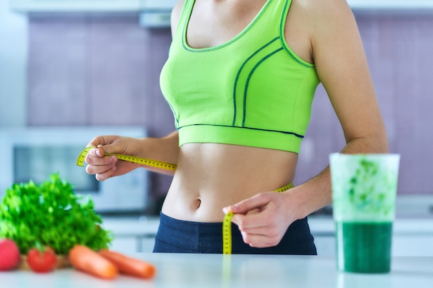 Dieet vrouw in sportkleding met meetlint en een groene smoothie voor afvallen.