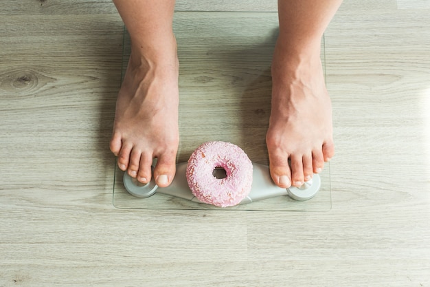 Dieetconcept. close-up van de voeten van de vrouw op weegschaal met donut. concept van snoep, ongezond junkfood en obesitas.