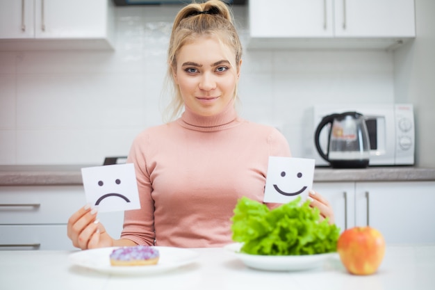 Dieetconcept, mooie jonge vrouw die tussen gezond voedsel en ongezonde kost kiezen