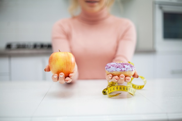 Dieetconcept, mooie jonge vrouw die tussen gezond voedsel en ongezonde kost kiezen