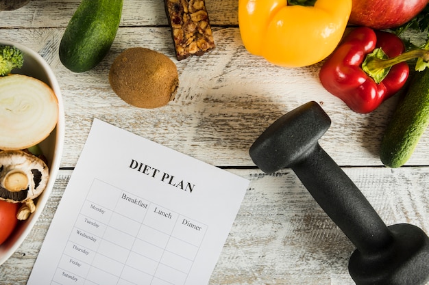 Foto dieetplan met groenten en halters op houten achtergrond