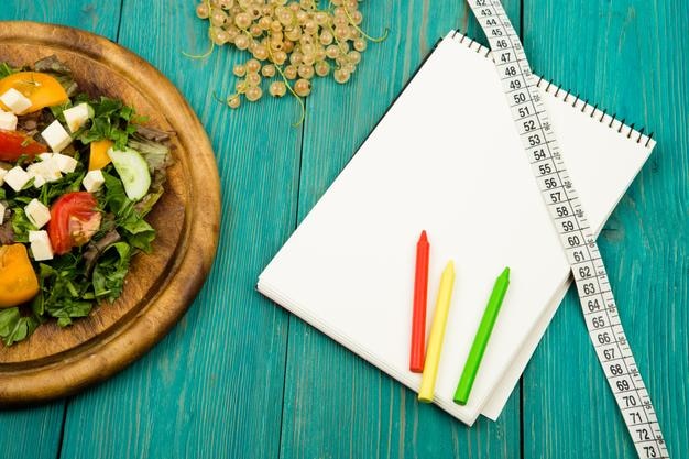 Dieetplansalade van meetlint met verse groenten en blanco notitieboekje op een witte houten tafel