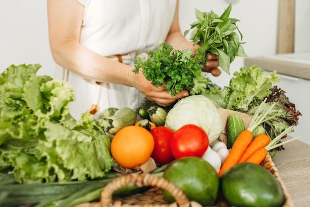 Dieetproducten Een vrouw houdt groen in haar handen tegen de achtergrond van groenten die op tafel liggen Gezonde voeding natuurlijke producten