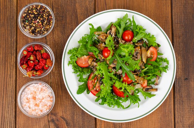 Dieetsalade van rucola-bladeren, tomaten en gebakken champignons op houten tafel.