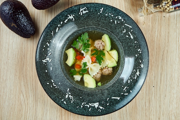 Dieetsoep met gehaktballen van kalkoen, avocado en pasta op houten tafel in zwarte kom. bovenaanzicht smakelijke soep. plat gelegd voedsel