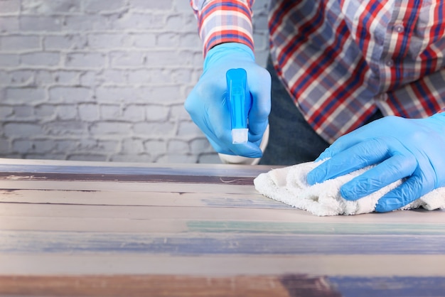 Dien blauwe rubberen handschoenen in met spuitfles en afvegen van een plat oppervlak