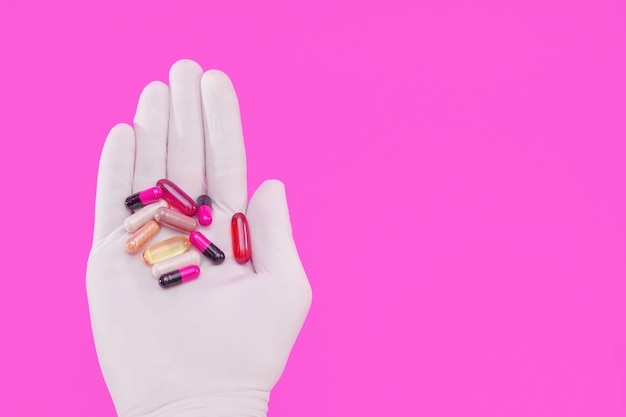 Dien een handschoen van veelkleurige pillen en capsules in op een roze achtergrond